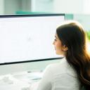 Portrait of Priya Shah reviewing a data model on a widescreen monitor in a bright office